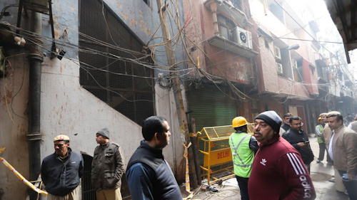 Policemen and neighbors stand in front of an ill-fated building which caught fire on Sunday, in New Delhi, India, Monday, Dec. 9, 2019. Authorities say an electrical short circuit appears to have caused a devastating fire that killed dozens of people in a crowded market area in central New Delhi. Firefighters fought the blaze from 100 yards away because it broke out in one of the area's many alleyways, tangled in electrical wire and too narrow for vehicles to access.