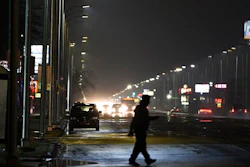 In this May 2, 2019, file photo, a pedestrian crosses Gratiot Street at Outer Drive East under a bright streetlight flanked by dimmer streetlights in Detroit. Leotek Electronics USA has agreed to pay $4 million to settle a lawsuit with Detroit over thousands of defective streetlights in Detroit, a newspaper reported. The city sued the company last spring, alleging that roughly 20,000 lights were failing.