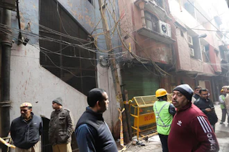 Policemen and neighbors stand in front of an ill-fated building which caught fire on Sunday, in New Delhi, India, Monday, Dec. 9, 2019. Authorities say an electrical short circuit appears to have caused a devastating fire that killed dozens of people in a crowded market area in central New Delhi. Firefighters fought the blaze from 100 yards away because it broke out in one of the area's many alleyways, tangled in electrical wire and too narrow for vehicles to access.