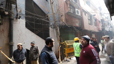 Policemen and neighbors stand in front of an ill-fated building which caught fire on Sunday, in New Delhi, India, Monday, Dec. 9, 2019. Authorities say an electrical short circuit appears to have caused a devastating fire that killed dozens of people in a crowded market area in central New Delhi. Firefighters fought the blaze from 100 yards away because it broke out in one of the area's many alleyways, tangled in electrical wire and too narrow for vehicles to access.