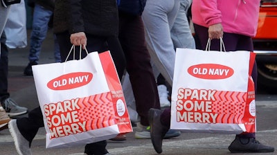 People carry shopping bags while crossing a street in San Francisco, Friday, Nov. 29, 2019. Black Friday once again kicked off the start of the holiday shopping season.