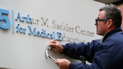 Worker Gabe Ryan removes a sign that includes the name Arthur M. Sackler at an entrance to Tufts School of Medicine, Thursday, Dec. 5, 2019, in Boston. Tufts University says it is stripping the Sackler name from its campus in recognition of the family's connection to the opioid crisis.