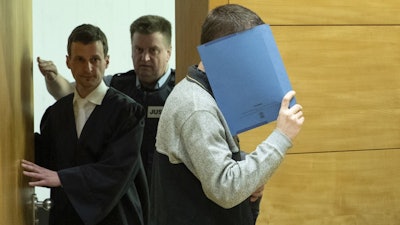 A 57-year old defendant hides his face at the courtroom in Bielefeld, Germany, Thursday, March 7, 2019. A judge in Germany has found the man guilty of poisoning his co-workers' sandwiches with mercury, lead acetate and other chemicals over several years and sentenced him to life in prison.