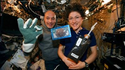 In this photo made available by U.S. astronaut Christina Koch via Twitter on Dec. 26, 2019, she and Italian astronaut Luca Parmitano pose for a photo with a cookie baked on the International Space Station. The results are finally in for the first chocolate chip cookie bake-off in space.