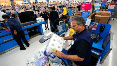 In this Nov. 9, 2018, file photo Walmart associate Javaid Vohar, right, checks out customers at a Walmart Supercenter in Houston. Walmart says it is testing higher wages for new hourly positions at 500 of its U.S. stores as part of an overall strategy to better empower its staff.