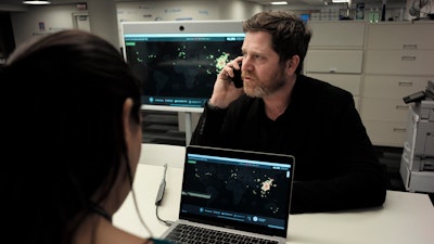 In this Thursday, Feb. 13, 2020 photo, John Brownstein, right, co-founder of HealthMap, a system using artificial intelligence to monitor global disease outbreaks, speaks on a phone in a HealthMap work area at Boston Children's Hospital in Boston.