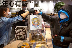 Manager Chen Tiantian, left, hands a takeaway order to a delivery driver at a Moka Bros cafe in Beijing on Friday, Feb. 14. For Valentine's Day Moka Bros, a health food eatery in Beijing, offered a special that included both a rose and a note logging the temperature of the chef that made the meal. Like many businesses in China, the restaurant has struggled to cope with the impact of a virus that has infected tens of thousands of people worldwide and sent several cities into lockdown.