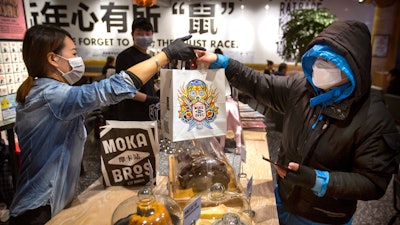 Manager Chen Tiantian, left, hands a takeaway order to a delivery driver at a Moka Bros cafe in Beijing on Friday, Feb. 14. For Valentine's Day Moka Bros, a health food eatery in Beijing, offered a special that included both a rose and a note logging the temperature of the chef that made the meal. Like many businesses in China, the restaurant has struggled to cope with the impact of a virus that has infected tens of thousands of people worldwide and sent several cities into lockdown.