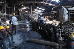 In this Sunday, Feb. 9, 2020 photo, Indian laborers sit near burnt remains after a fire broke out at Nandan Denim, one of the largest denim suppliers in the world, in Ahmedabad, India. At least seven people died in the blaze that swept the factory that has ties to major U.S. retailers, according to its website. Some of the U.S. and multinational companies listed on the website said they were not actually customers, and many issued statements that strongly condemned dangerous work sites.