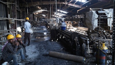 In this Sunday, Feb. 9, 2020 photo, Indian laborers sit near burnt remains after a fire broke out at Nandan Denim, one of the largest denim suppliers in the world, in Ahmedabad, India. At least seven people died in the blaze that swept the factory that has ties to major U.S. retailers, according to its website. Some of the U.S. and multinational companies listed on the website said they were not actually customers, and many issued statements that strongly condemned dangerous work sites.