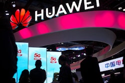 In this Oct. 31, 2019, file photo, attendees walk past a display for 5G services from Chinese technology firm Huawei at the PT Expo in Beijing. Chinese smartphone brand Huawei says it will attend the industry’s biggest global event this month in Barcelona while more companies reported losses due to China’s efforts to contain a disease outbreak.