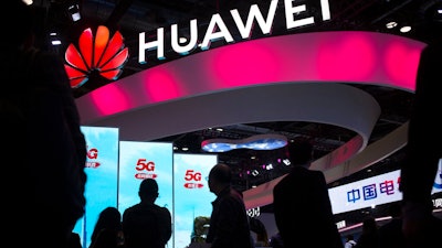 In this Oct. 31, 2019, file photo, attendees walk past a display for 5G services from Chinese technology firm Huawei at the PT Expo in Beijing. Chinese smartphone brand Huawei says it will attend the industry’s biggest global event this month in Barcelona while more companies reported losses due to China’s efforts to contain a disease outbreak.