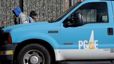 In this photo taken Feb. 18, 2020, people walk behind a Pacific Gas and Electric truck parked in San Francisco.