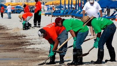 In this June 12, 2010, file photo, oil cleanup workers hired by BP clean oily deposits from the shore in Orange Beach, Ala. The spring of coronavirus feels a lot like the summer of oil to residents along the Gulf Coast. Bars and restaurants are empty in Florida because of an invisible threat nearly a decade after the BP oil spill ravaged the region from the ocean floor up, and condominium reservations have taken a nosedive in Alabama.