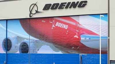 A worker walks near a mural of a Boeing 747-8 airplane at the company's manufacturing facility in Everett, Wash., Monday, March 23, 2020, north of Seattle. Boeing announced Monday that it will be suspending operations and production at its Seattle area facilities due to the spread of the new coronavirus.
