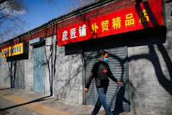 A man wearing a protective face mask walks by shuttered business shops in Beijing, Sunday, March 1, 2020. Amid fears about where the next outbreak of a fast-spreading new virus would appear, infections and deaths continued to rise across the globe Sunday, emptying streets of tourists and workers, shaking economies and rewriting the realities of daily life.