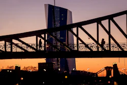 Two women walk over a bridge with the European Central Bank in background in Frankfurt, Germany, as the sun rises Monday, March 30, 2020.