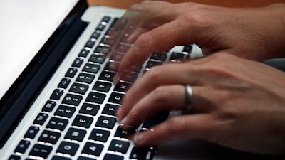 This June 19, 2017 file photo shows a person working on a laptop in North Andover, Mass. The U.S. internet won’t get overloaded by spikes in traffic from the millions of Americans now working from home to discourage the spread of the new coronavirus, experts say. But connections could stumble for many if too many family members try to videoconference at the same time.