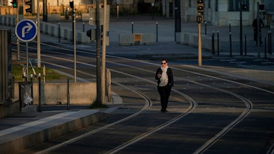 A woman walks on empty tram rails in Lyon, central France, Monday, March 23, 2020. French citizens are only allowed to leave their homes for necessary activities such as shopping for food, going to work or taking a quick walk due to the rapid spreading of the new coronavirus in the country. For most people, the new coronavirus causes only mild or moderate symptoms. For some it can cause more severe illness, especially in older adults and people with existing health problems.