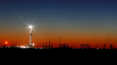 In this Thursday, April 2, 2020 photo, an oil rig lights up the horizon on the outskirts of Midland, Texas after a late sunset.