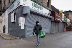In this Friday, April 3, 2020, photo, a woman walks by local stores during the coronavirus pandemic in New York.