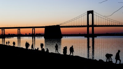 People gather to watch the sun set behind the Throgs Neck Bridge at LIttle Bay Park Wednesday, April 8, 2020, in the Queens borough of New York. While New York Gov. Andrew Cuomo said New York could be reaching a 'plateau' in hospitalizations, he warned that gains are dependent on people continuing to practice social distancing.