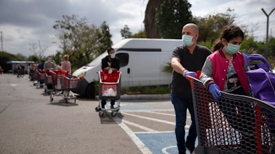 Customers wear face masks as they line up to enter a supermarket keeping social distancing following the government's measures to help stop the spread of the coronavirus, in Tel Aviv, Israel, Tuesday, April 7, 2020. Israeli Prime Minister Benjamin Netanyahu announced Monday a complete lockdown over the upcoming Passover holiday to control the country's coronavirus outbreak, but offered citizens some hope by saying he expects to lift widespread restrictions after the week-long festival.