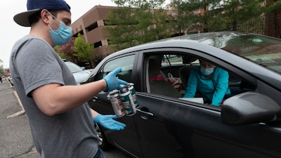 In this May 8 photo, Jack's Abby craft brewery employee Casey Mott carries an order to a customer in a line of cars waiting curbside in Framingham, MA.