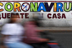 In this April 28, 2020 photo, a couple rides a motorcycle past a painted sign reading in Spanish 'Coronavirus. Stay Home,' in Iztapalapa, Mexico City. Mexico has had extremely limited testing compared with other countries, another factor that experts have said made it difficult for the country to contain the virus.