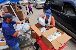 Wearing masks amid concerns of the spread of COVID-19, volunteers Karen Cooperstein, right, and Edwin Chinchilla, left, prepare food for the pubic during a drive through food pantry distribution by Catholic Charities in Dallas, Thursday, July 2, 2020.
