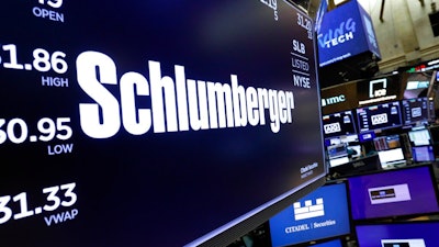 In this Oct. 8, 2019 file photo, the logo for Schlumberger appears above a trading post on the floor of the New York Stock Exchange. Schlumberger is cutting more than 21,000 jobs and paying $1.02 billion in severance as declining oil prices amid the coronavirus pandemic push it to slash costs Schlumberger Ltd. said in a regulatory filing on Friday, July 24, 2020, that vast majority of the severance charge is expected to be paid out during the second half of the year.