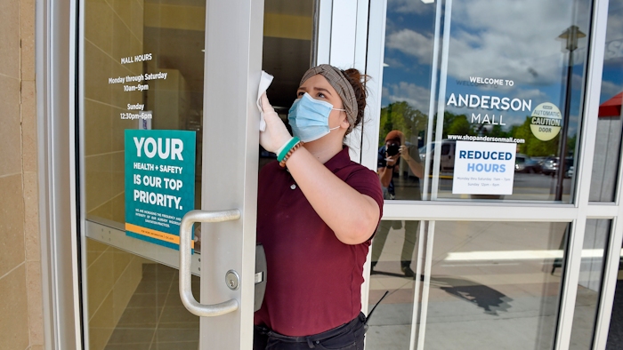 Kendall Ballew, an employee of the Anderson Mall, cleans the doors before the mall opened to limited business in Anderson, S.C.