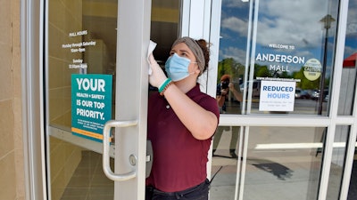 Kendall Ballew, an employee of the Anderson Mall, cleans the doors before the mall opened to limited business in Anderson, S.C.