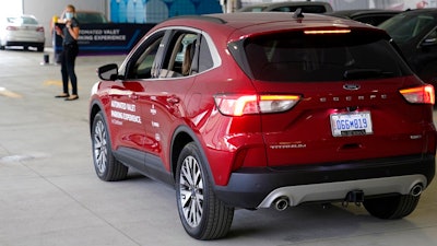 A Ford Escape automatically stops as a pedestrian crosses in front during a self park demonstration, Tuesday, Aug. 25, 2020 in Detroit. Ford, Bosch and real estate company Bedrock are teaming up to test technology that will let vehicles park by themselves in parking decks. The companies are testing the technology using floor-mounted sensors and computers that can control mainly existing features in the Ford Escape. They say the technology is likely to arrive before widespread use of fully autonomous vehicles because sensors and computers inside parking decks can be used.