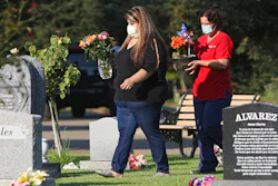 Lori Gonzalez, left, and Rachel Spray carry flowers to the temporary grave marker of Gonzalez's sister and Kaiser Permanente Fresno Medical Center nurse, Sandra Oldfield, at the Sanger Cemetery in Sanger, Calif., Saturday, Aug. 29, 2020.