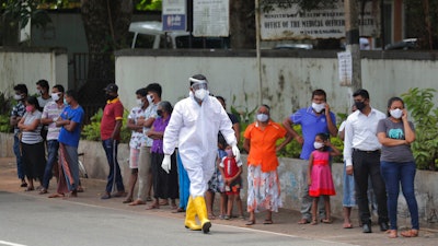 Sri Lankans wait to give swab samples to test for COVID-19 outside a hospital as a health official walks past in Minuwangoda, Sri Lanka.