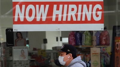 A man wearing a mask while walking under a Now Hiring sign at a CVS Pharmacy.