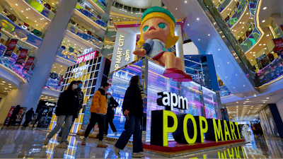 Shoppers wearing face masks to help curb the spread of the coronavirus wall by the Chinese toy maker POP Mart display booth at a shopping mall in Beijing on Dec. 9, 2020.