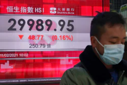 A man wearing a face mask walks past a bank's electronic board showing the Hong Kong share index in Hong Kong, Thursday, Feb. 11, 2021. Despite a short drop in early trading in Hong Kong, most major Asian stock indexes were higher on Thursday after President Joe Biden held his first conversation with Chinese leader Xi Jinping since taking office.