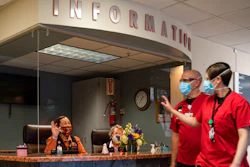 Medical Center Hospital auxiliary volunteers Gracie Sanchez, seated left, and Ann Ellison wave at passing health care workers as they work at Medical Center Hospital's information desk, Wednesday, March 10, 2021, in Odessa, Texas. In addition to wearing masks and remaining behind a plexiglass protective shield, the volunteers are required to have had a COVID-19 vaccine or be able to prove they have antibodies to the virus before returning to volunteer in person.