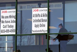 In this file photo, a woman, wearing a protective mask due to the COVID-19 virus outbreak, walks past the signs of an employment agency, in Manchester, NH.