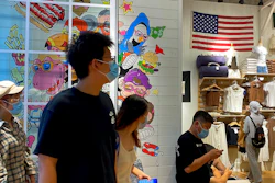People wearing face masks visit a fashion boutique displaying an American flag in Beijing, Sunday, July 11, 2021. China on Sunday said it will take 'necessary measures' to respond to the U.S. blacklisting of Chinese companies over their alleged role in abuses of Uyghur people and other Muslim ethnic minorities.