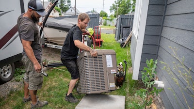 Carl Rocha, left, and Patrick Plummer, with Bills Heating & A/C Install air conditioning and a new furnace at a home on East Wabash Street, Wednesday, June 23, 2021, in Spokane, Wash.