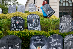 Jayde Newton helps to set up cardboard gravestones with the names of victims of opioid abuse outside the courthouse where the Purdue Pharma bankruptcy is taking place in White Plains, N.Y., Monday, Aug. 9, 2021. Purdue Pharma's quest to settle thousands of lawsuits over the toll of OxyContin is entering its final phase with the grudging acceptance of most of those with claims against the company.
