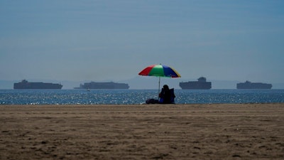A beach goer sits on the beach in Seal Beach Calif., Friday, Oct. 1, 2021, as container ships waiting to dock at the Ports of Los Angeles and Long Beach are seen in the distance. With three months until Christmas, toy companies are racing to get their toys onto store shelves as they face a severe supply network crunch. Toy makers are feverishly trying to find containers to ship their goods while searching for new alternative routes and ports.