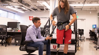 University of Utah mechanical engineering assistant professor Tommaso Lenzi, left, helps Alec McMorris put on an experimental exoskeleton that Lenzi has developed for lower-limb amputees.