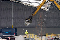 Workers use equipment to remove a section of roof left on a heavily damaged Amazon fulfillment center on Dec. 11, 2021 in Edwardsville, IL.