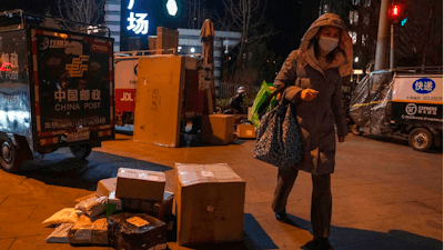 A woman wearing a mask to protect from the coronavirus walks past parcels gathered near delivery tricycles in Beijing, China, Tuesday, Jan. 18, 2022. Chinese state media say parcels mailed from overseas may have spread the omicron variant of the coronavirus in Beijing and elsewhere, despite doubts among overseas health experts that the virus can be transmitted via packaging.