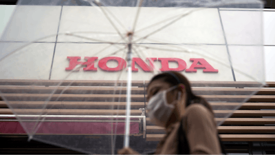 A woman walks in the rain near the logo of Honda Motor Company Friday, May 13, 2022, in Tokyo. Honda’s fiscal fourth quarter profit slipped to almost half of what the Japanese automaker earned the previous year amid headwinds of supply shortages and rising raw material costs.