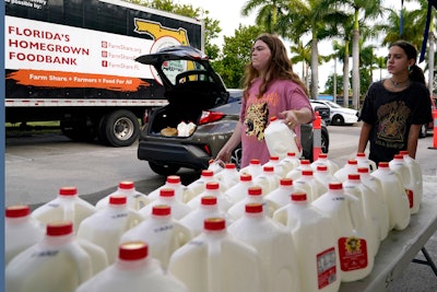 Vanessa Correa, left, and Gigi Fiske, right, pass out gallons of milk at a food distribution held by the Farm Share food bank, Wednesday, July 20, 2022, in Miami. Long lines are back at food banks around the U.S. as working Americans overwhelmed by inflation turn to handouts to help feed their families.